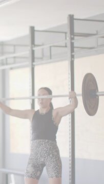 Vertical video: Woman lifter stabilizing bar overhead, lowering it to reset lift on fitness rig