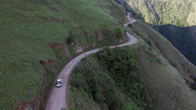 Aerial follows truck driving up dirt road on steep mountainside slope
