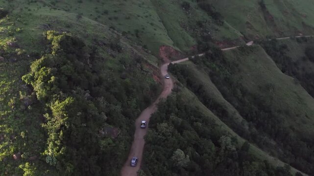 Vehicles drive on gravel road contouring up steep mountain slope