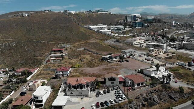 Aerial drone shot of hillside residential area with houses, roads and parked cars, dry terrain and scattered buildings showing suburban development and elevated landscape view