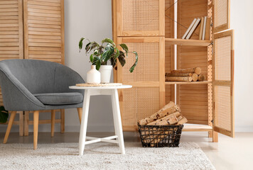 Naklejka premium Interior of living room with armchair, closet, folding screen, coffee table and firewood in basket