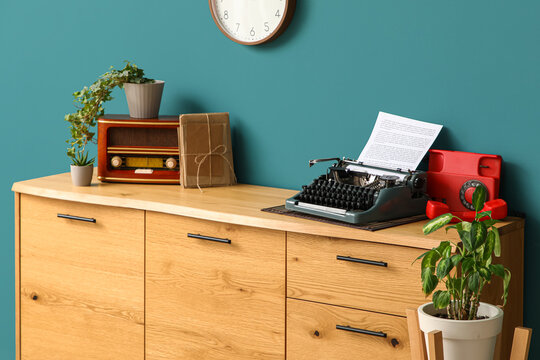 Vintage typewriter, telephone and radio receiver on wooden chest of drawers in interior of living room, closeup