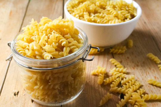 fusilli pasta in a jar and bowl on a wooden table