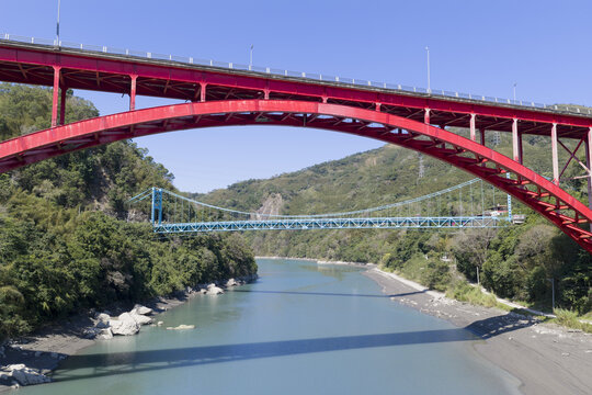 Aerial view of the vibrant red Luofu Bridge and the blue Fuxing Bridge spanning the Dahan River surrounded by lush green mountains Fuxing District, Taoyuan City, Taiwan.