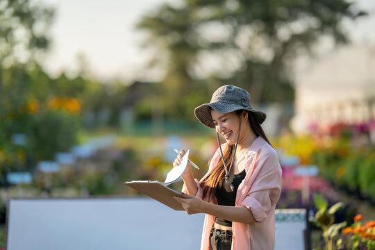 Woman gardener smiling writing on clipboard in plant nursery