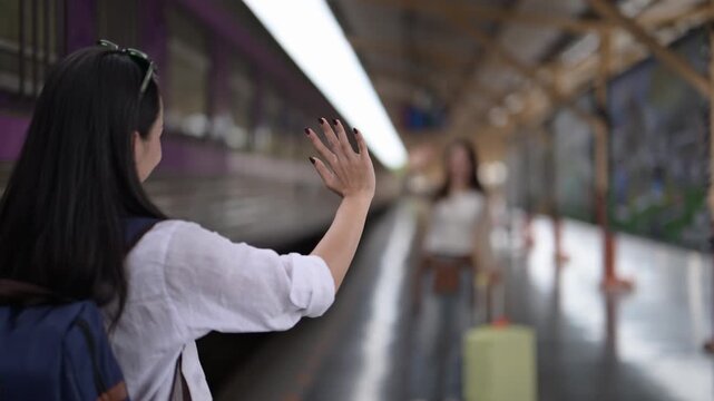 woman is waving to another woman at a train station. The woman is wearing a white shirt and has a backpack on her back