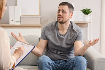 Fototapeta premium Male drug addict talking to psychologist on sofa in office