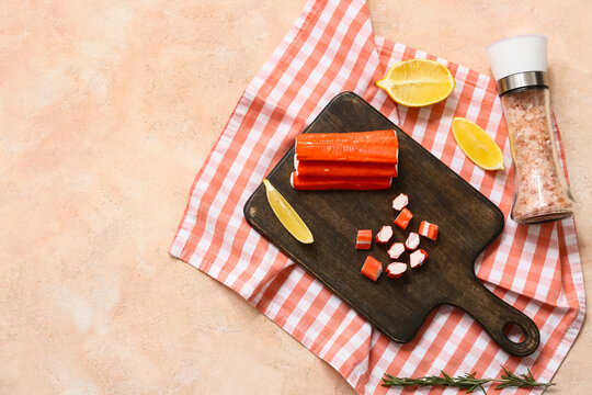 Wooden board with tasty crab sticks and cut lemon on beige background