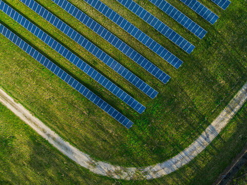 Aerial view of rows of blue solar panels installed on a lush green field with a curved dirt path under bright sunlight in Indianapolis, Indiana, United States.