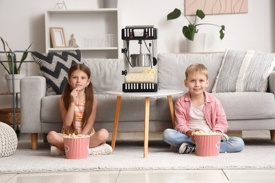 Little children with popcorn machine watching movie at home