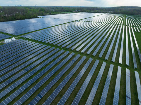 Aerial view of a vast solar farm with rows of photovoltaic panels reflecting sunlight surrounded by lush green trees and fields in Indianapolis, Indiana, United States.