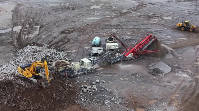 Aerial view of a vibrating screen stone crusher in operation at an industrial quarry near Halifax, Nova Scotia, Canada. Heavy machinery processes stone into aggregates for construction 4K.