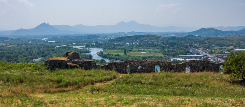 A broad panoramic vista from Rozafa Castle ruins, revealing the winding Buna River, expansive green valley, and distant mountain ranges in Shkoder, Albania.