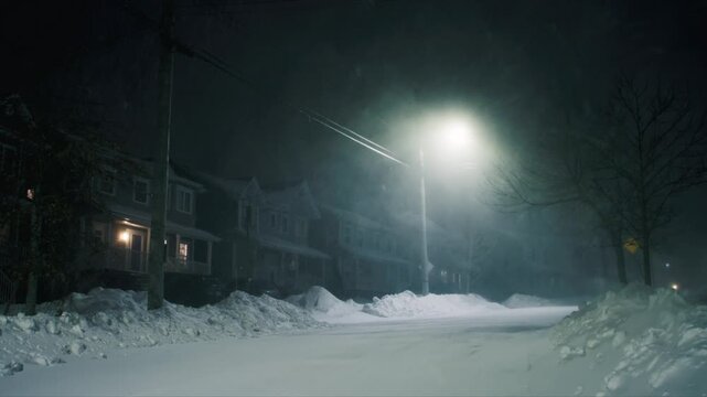 Atmospheric night scene during intense snowstorm with strong winds in Beechville near Halifax. Snow rapidly accumulates into large drifts blocking the road and sidewalks, streetlights barely visible