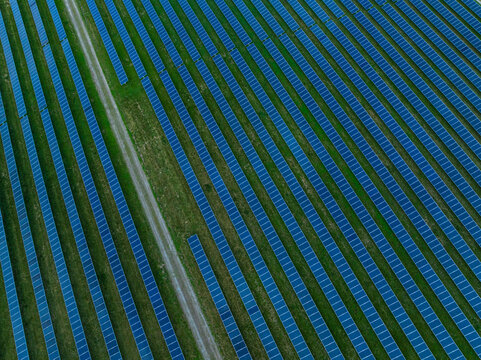 Aerial view of rows of blue solar panels arranged in a geometric pattern on a green field with a dirt access road Indianapolis, Indiana, United States.