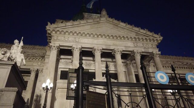 Argentine National Congress Palace in Buenos Aires. Illuminated at night behind iron gates with national cockades