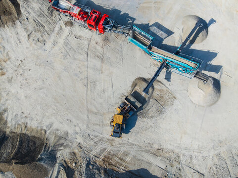 Aerial view of heavy industrial machinery including a red crusher and yellow loader operating at a gravel quarry site in Indianapolis, Indiana, United States.