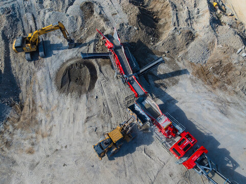 Aerial view of heavy machinery including an excavator and a mobile crusher operating on a dusty construction site with piles of gravel Indianapolis, Indiana, United States.