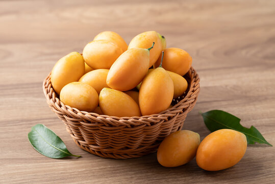 Fresh Marian plum (Mayongchid) in a wicker basket on wooden background, Thai tropical fruit in summer season