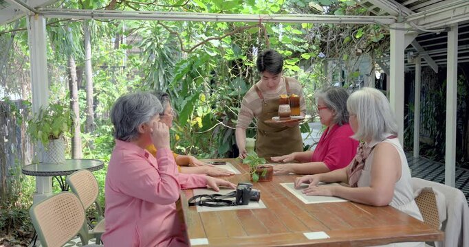 Senior Asian women friends ordering drinks at outdoor cafe reunion, retired female group welcoming service, sharing conversation, togetherness, relaxation, friendship bonding during cafe gathering