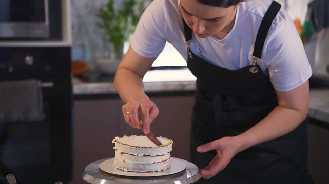 Young baker focuses intently on cake decoration. Hands glide carefully over layers with a spreading tool. Each motion reflects precision and care. Ideal for culinary or baking tutorials