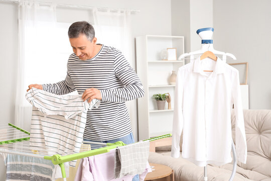 Mature man taking laundry from dryer and steamer at home