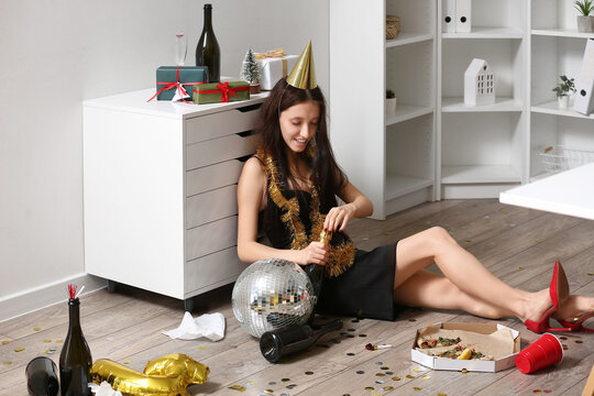 Drunk young woman opening bottle of champagne in office after New Year party