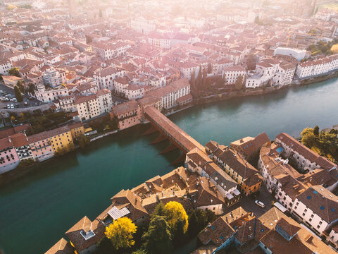 Aerial view of the historic Ponte degli Alpini bridge spanning the Brenta River surrounded by traditional terracotta rooftops in the soft morning light in Bassano del Grappa, Veneto, Italy.