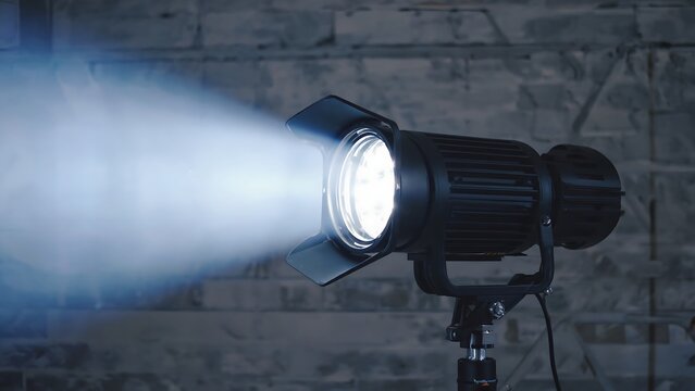 Studio lighting setup with a fresnel light emitting a bright beam against a brick wall backdrop.