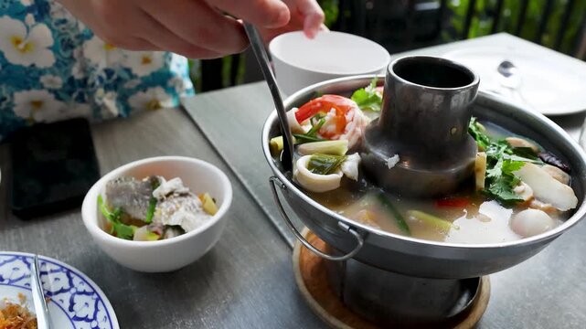 Serving Traditional Thai Tom Yum Seafood Soup in a Metal Hot Pot