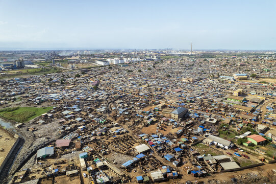 Aerial view of the dense residential area near Fishing Harbour Road with industrial facilities and storage tanks in the background under a clear sky in Tema, Greater Accra Region, Ghana.
