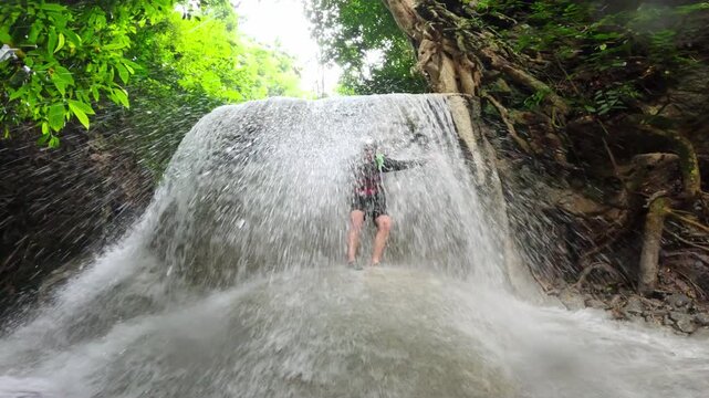 Man stands under Aguinid Falls enjoying strong water flow, splashes, Philippines