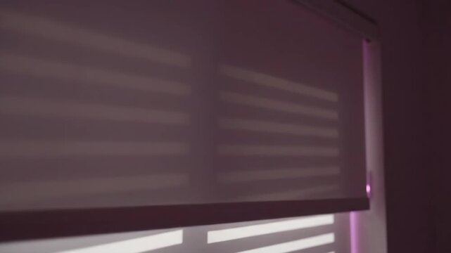 Natural light streaming through window blinds, casting geometric stripes of shadow and bright illumination. A minimalist indoor scene showcasing architectural patterns on a serene daytime background.