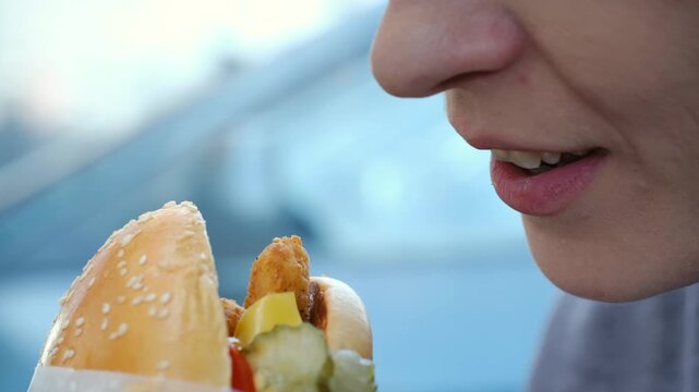 Extreme close up woman face enjoys delicious aroma of freshly prepared fish burger before taking big bite, savoring taste of her fast food meal. Close up hungry woman smelling and eating fish sandwich