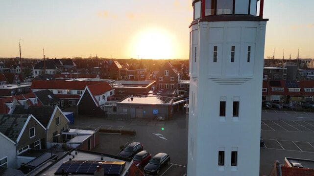 Drone descends beside the lighthouse from bright backlight toward the entrance level.