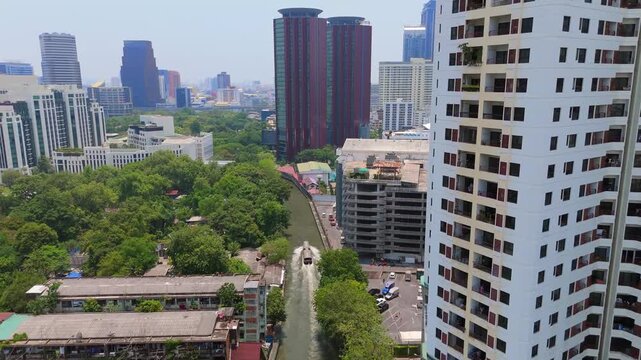 Drone view of Khlong Saen Saep in Asoke showing canal boat moving through waterway greenery along banks and surrounding high rise buildings in dense urban district