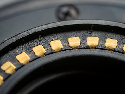 macro closeup of gold plated electronic contacts on a camera lens bayonet mount against blurred black plastic parts
