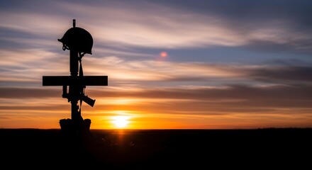 Obraz premium Silhouette of a fallen soldier memorial with rifle, helmet, and boots against a dramatic sunset sky, representing military sacrifice, remembrance, honor, and respect for veterans in a peaceful
