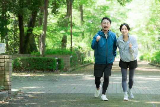 新緑の公園でウォーキングやランニングのスポーツが楽しいミドル夫婦の正面カメラ目線笑顔　ダイエットや健康などの明るいイメージ全身