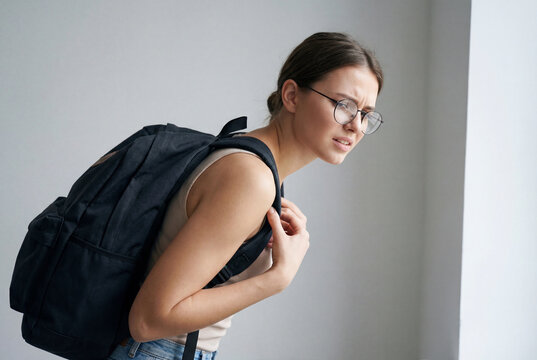 Student with glasses suffering from back pain due to a very heavy backpack