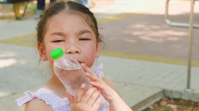 Young Thai Girl Cooling Her Cheek with a Cold Water Bottle Outdoors