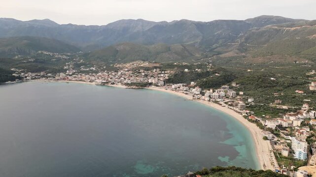 Scenic aerial fly over view gentle calm waves and pebbled shoreline at Himara Beach along the stunning Albanian Riviera. A perfect relaxing Mediterranean travel destination in EUROPE