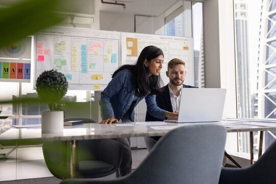 Multiethnic colleagues working together on project or presentation, review new platform, discussing content, pitch deck, proposal or analytics report using modern laptop during collaborative workflow