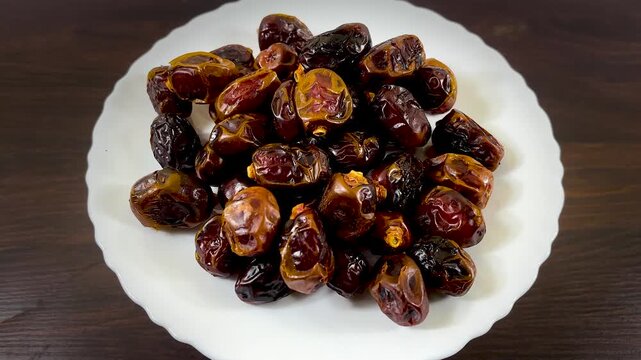 Dried date fruit on white plate, organic sweet dates for ramadan, pile of brown sticky date palm fruits on wooden table