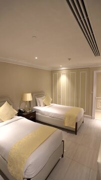 A clean, modern hotel room featuring two single beds with white linens and elegant yellow throw pillows and runners.