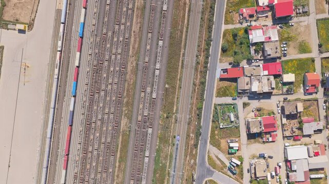 Aerial perspective showing a passenger train moving along the tracks of a large railway station, passing numerous freight trains and wagons parked on parallel tracks next to a small town