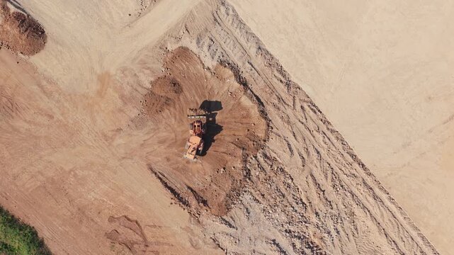 Rising aerial view captures a powerful bulldozer leveling earth, revealing a waiting dump truck and the expansive scope of a massive industrial development site.