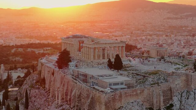 Breathtaking aerial view of the ancient acropolis in athens, with the majestic parthenon illuminated by a warm, golden sunset, showcasing the historic cityscape and surrounding mountains