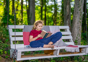 Fototapeta premium Carefree child resting on swing in backyard. Kid sitting relaxed and joyful on swing. Young child enjoying leisure and playful activity outdoors. Boy swinging calmly in green garden.