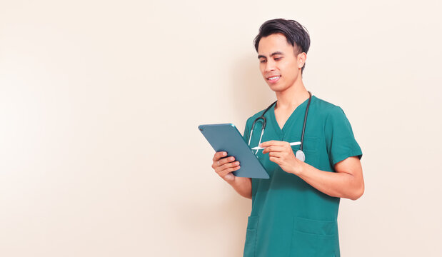 Smiling Southeast Asian male nurse or doctor in green scrubs holding a digital tablet. Professional healthcare worker presenting medical information or digital records on isolated background.